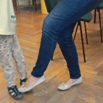 Warsztaty rodzinne "Poznajemy emocje z Kamą Lamą" - dziecko wykonuje ćwiczenie ruchowe wspólnie z osobą dorosłą, unosząc nogę i naśladując prezentowany ruch.