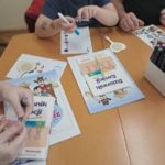Terapia ręki - konsultacje - dzieci podczas zajęć przy stole wykonują zadania z wykorzystaniem kart pracy, flamastrów, naklejek i innych materiałów edukacyjnych.